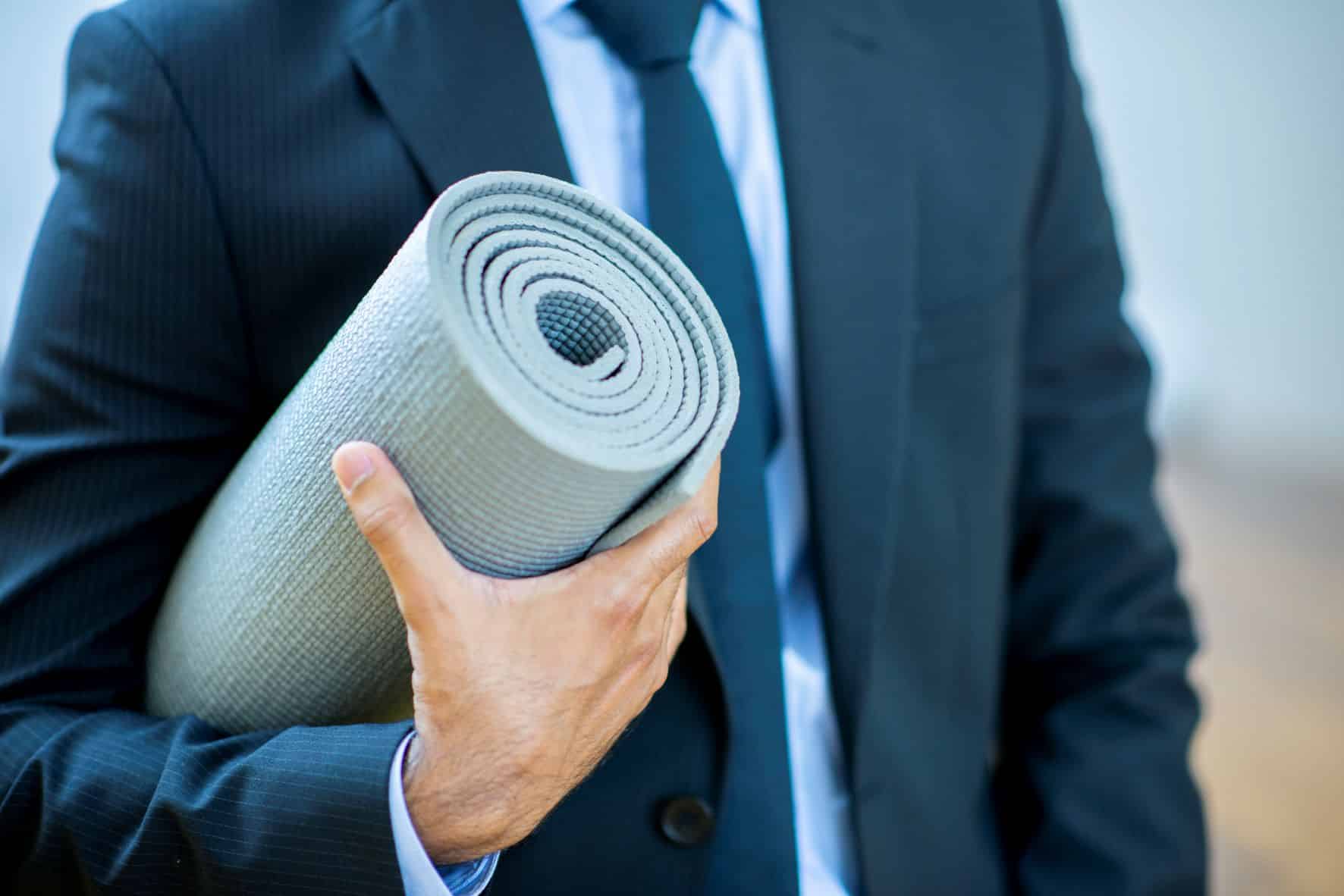 Homme en costume avec tapis de yoga sous le bras
